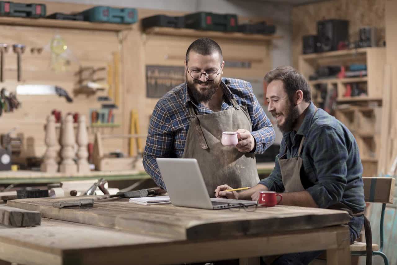 Two wood designer working with laptop in workshop.